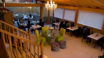 A dining area with round tables, green chairs, zebra-patterned ottomans, and a chandelier.
