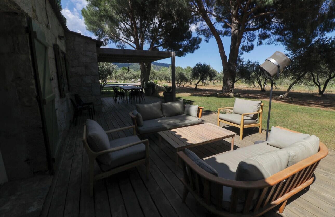 An outdoor deck with wooden furniture, including sofas and chairs, and a pergola structure.