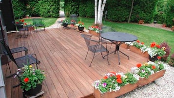 A wooden deck with outdoor furniture, surrounded by flower planters and a grassy area.