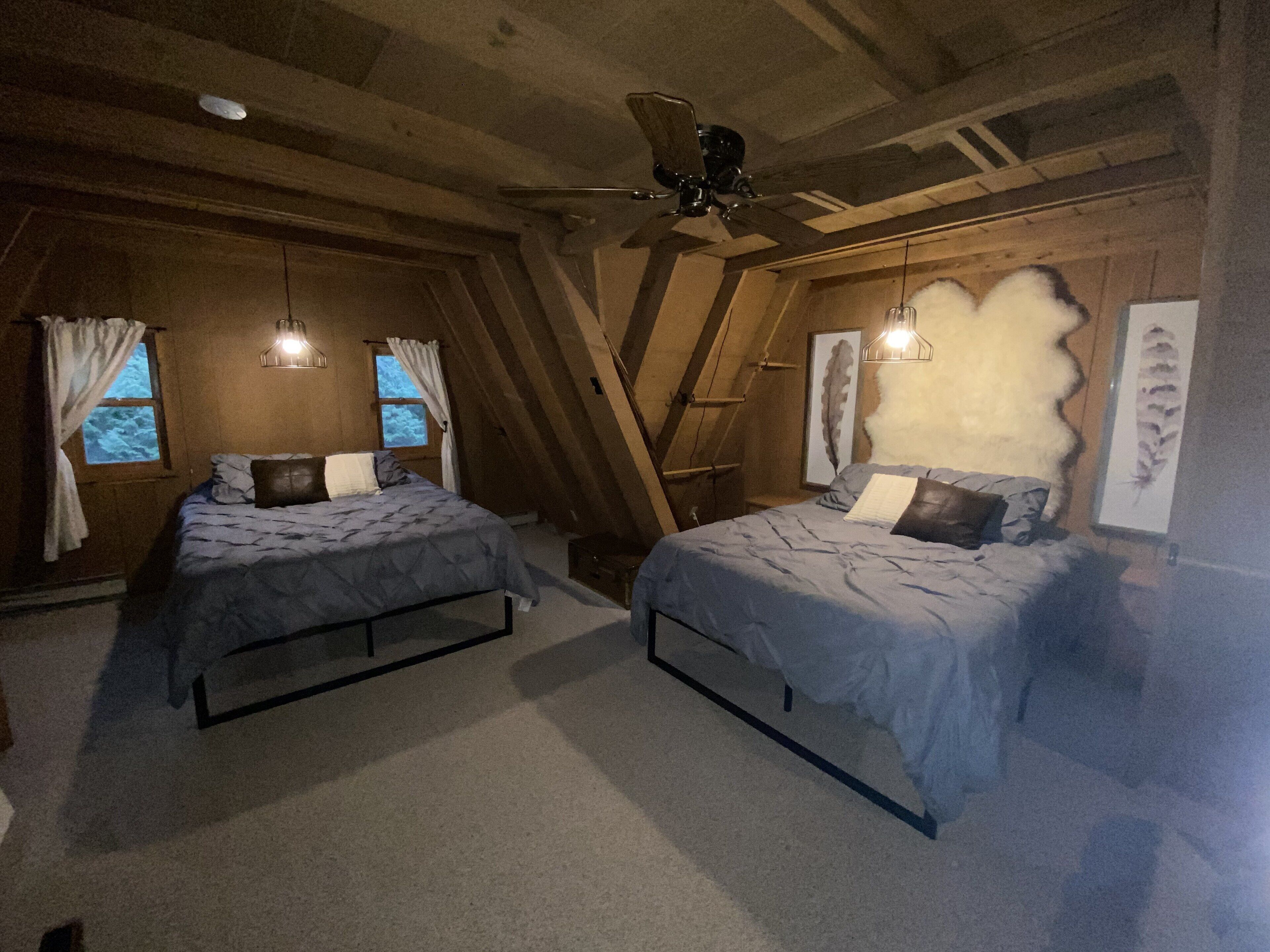 A bedroom with two beds, wooden walls, a ceiling fan, and a window with curtains.
