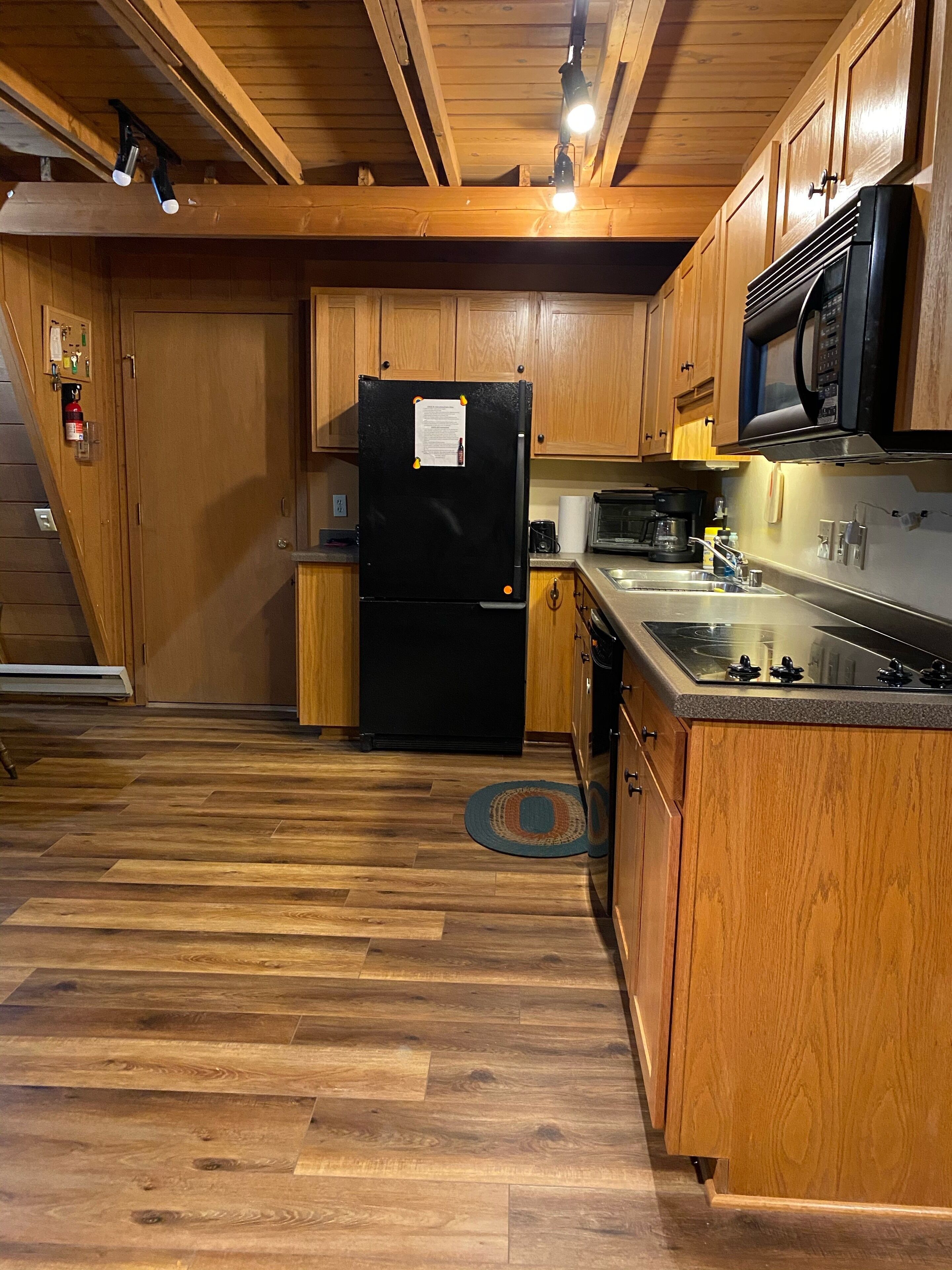 Una cocina compacta con armarios de madera, un refrigerador negro, un microondas y una estufa.