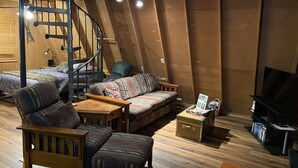 Acogedor apartamento estilo loft con una escalera de caracol, un conjunto de sofás, un banco de madera, una mesita y un televisor.