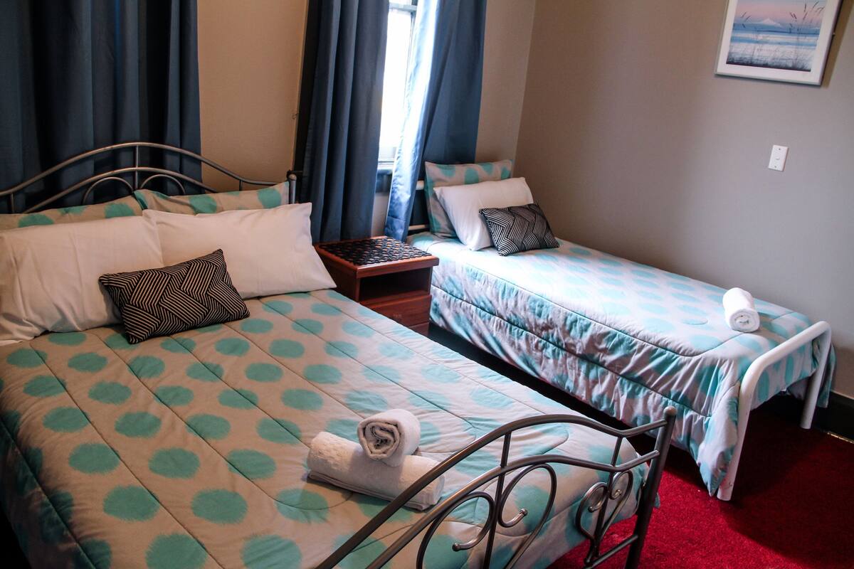 Une chambre avec deux lits, chacun étant agrémenté d’une couvre-lit et de coussins à motifs. Une petite table avec une lampe se trouve entre les deux lits.