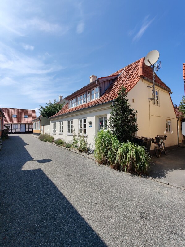 Une maison à deux étages, avec un toit recouvert de tuiles rouges, une antenne parabolique et une allée gravillonnée.