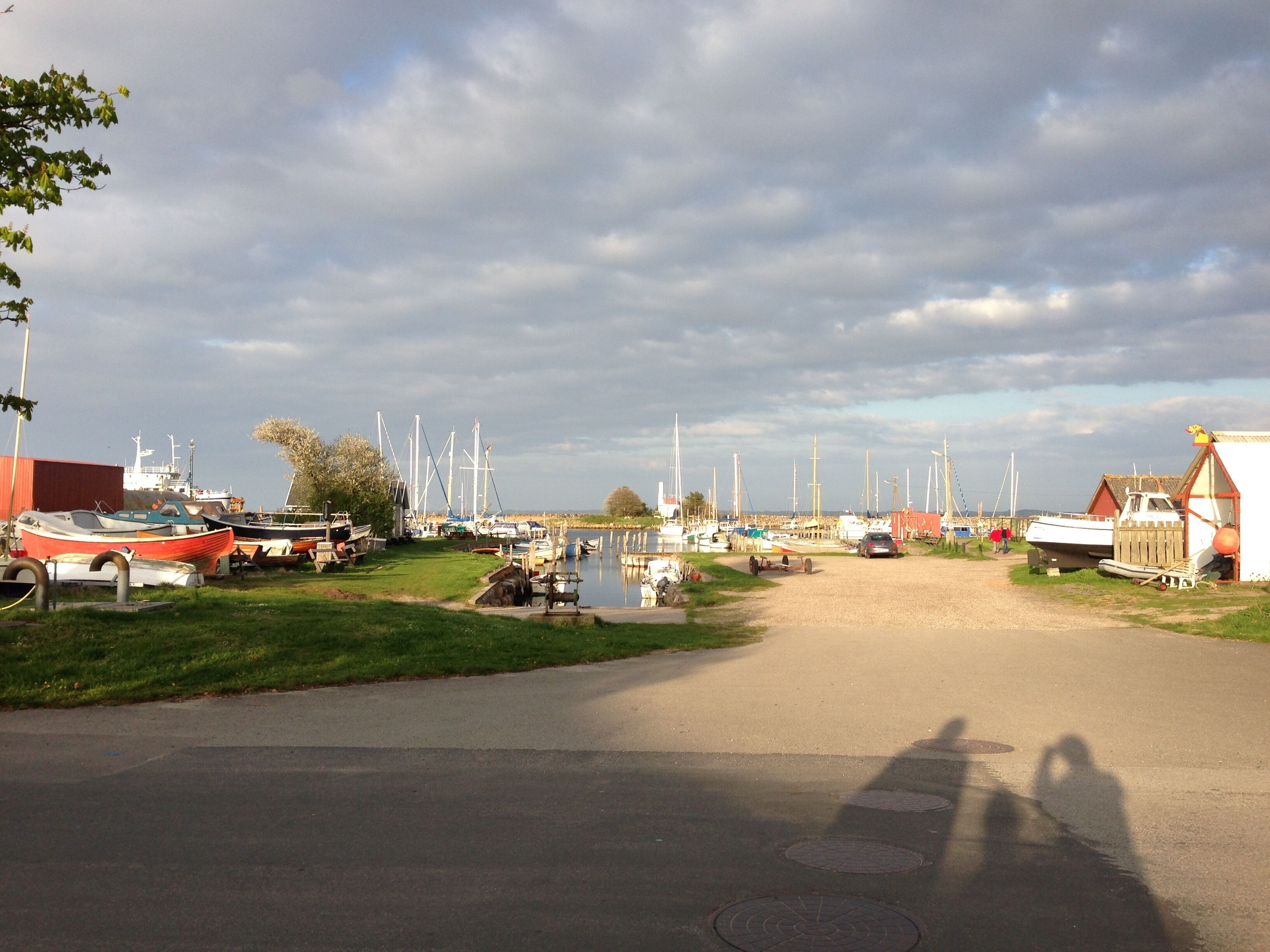 A marina with boats docked, a dirt path leading to the water, and a red building on the left.