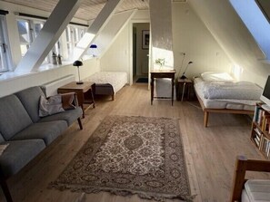 Une chambre mansardée chaleureuse avec un plafond en pente, une grande fenêtre, un lit, un bureau, une chaise et un canapé.