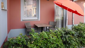 A small outdoor seating area with a table and two wicker chairs, a red umbrella, and a window with a view of buildings. - Typically Saxon! Cozy little apartment in the heart of Dresden. (Dresden)