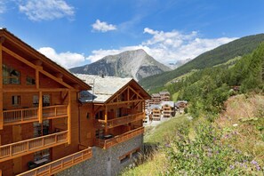 Un chalet en bois doté de balcons, avec une base en pierre et un paysage montagneux en arrière-plan.