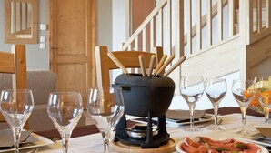 Una mesa de comedor dispuesta con copas de vino, una olla negra con palitos de madera y platos de comida.