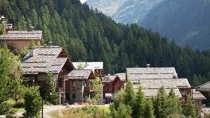 Un pueblo de montaña con casas de madera tradicionales, un edificio de piedra y un paisaje boscoso al fondo.