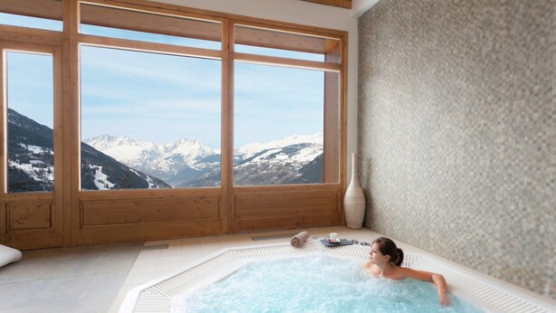 Un cuarto de spa con hidromasaje, marcos de ventana de madera y vistas a montañas nevadas.
