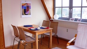 Ein Essbereich mit Holztisch und Korbstühlen, ein Fenster mit Blick und ein Poster an der Wand.