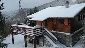 Uma cabana com base de pedra e fachada de madeira, rodeada por árvores e montanhas cobertas de neve.