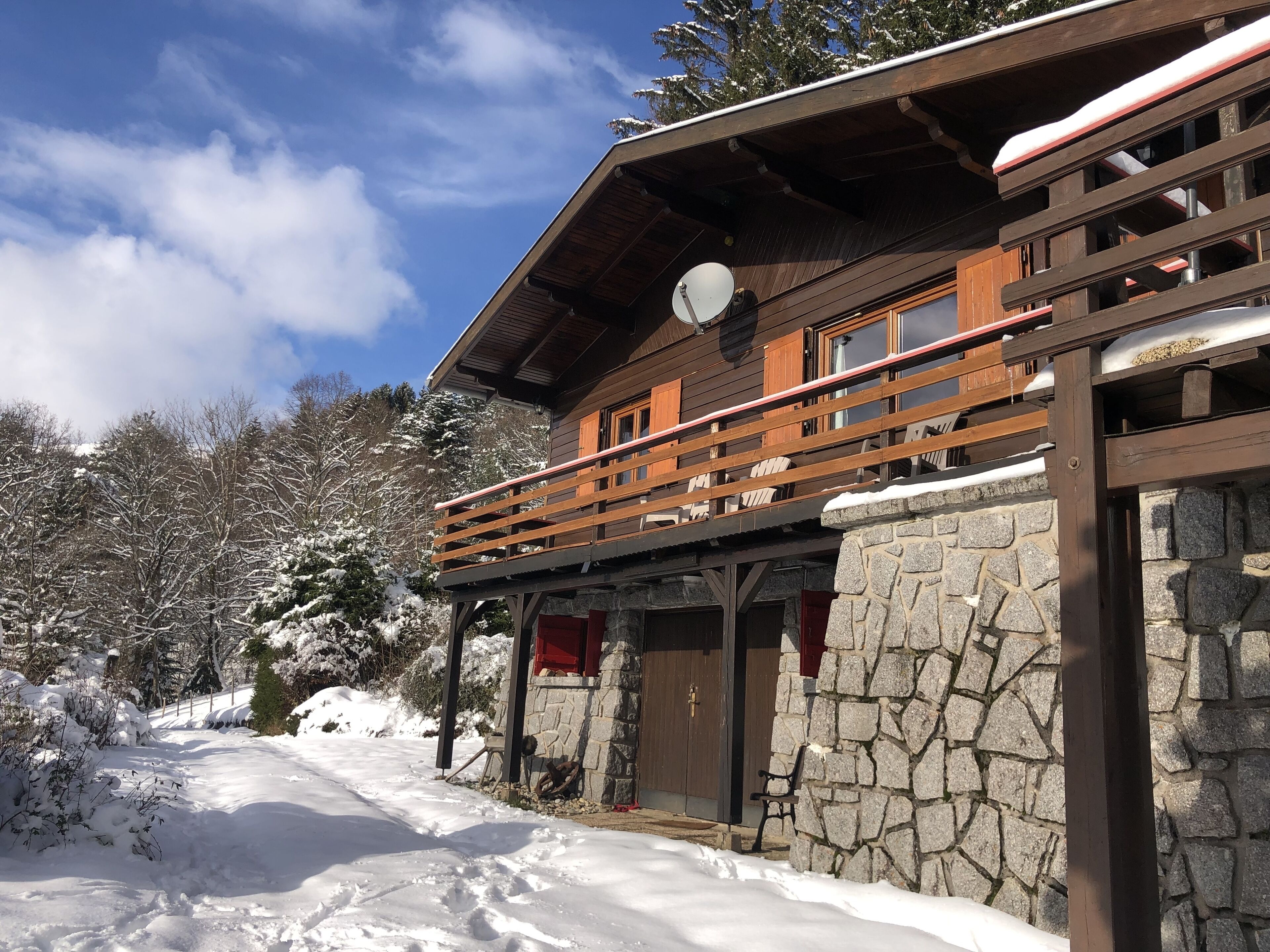 A wooden cabin with a stone exterior, a balcony, and a stone wall.