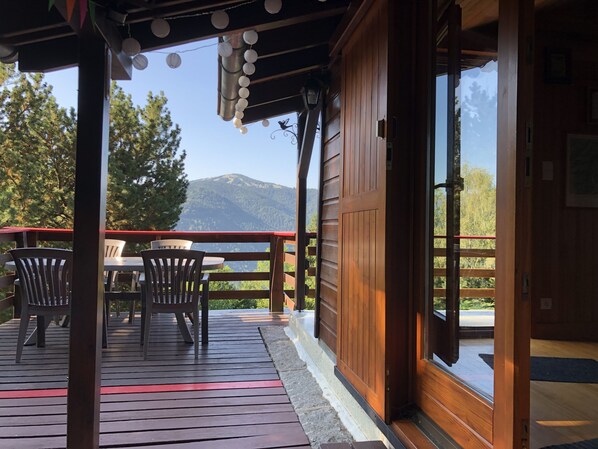 Una terraza de madera con sillas y una mesa, con vistas a un paisaje montañoso.