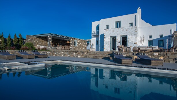 A modern building with a pool, stone walls, and outdoor seating. - Aelia Luxury Villa with Sea view and swimming Pool (Paros)