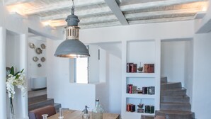 A modern interior with a wooden dining table, cushioned seating, a hanging pendant light, and a staircase leading to an upper level. - Aelia Luxury Villa with Sea view and swimming Pool (Paros)