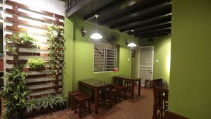 A dining area with wooden tables and chairs, a green wall, and hanging plants. - Hanoi Balcony Homestay (Hanoi)