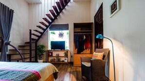 A bedroom with a bed, a TV on a stand, a chair, a floor lamp, and a staircase leading to a closet. - Hanoi Balcony Homestay (Hanoi)