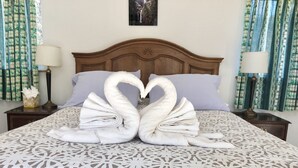Ein Bett mit einem gemusterten Überwurf, einem Holz-Kopfteil und zwei Handtüchern, die zu einem Herz geformt sind.