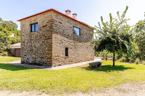 A stone house with a red-tiled roof, two windows, and a paved entrance.