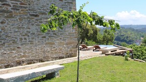 A stone building with a red-tiled roof, a small tree in front, and a clear view of the landscape in the background.