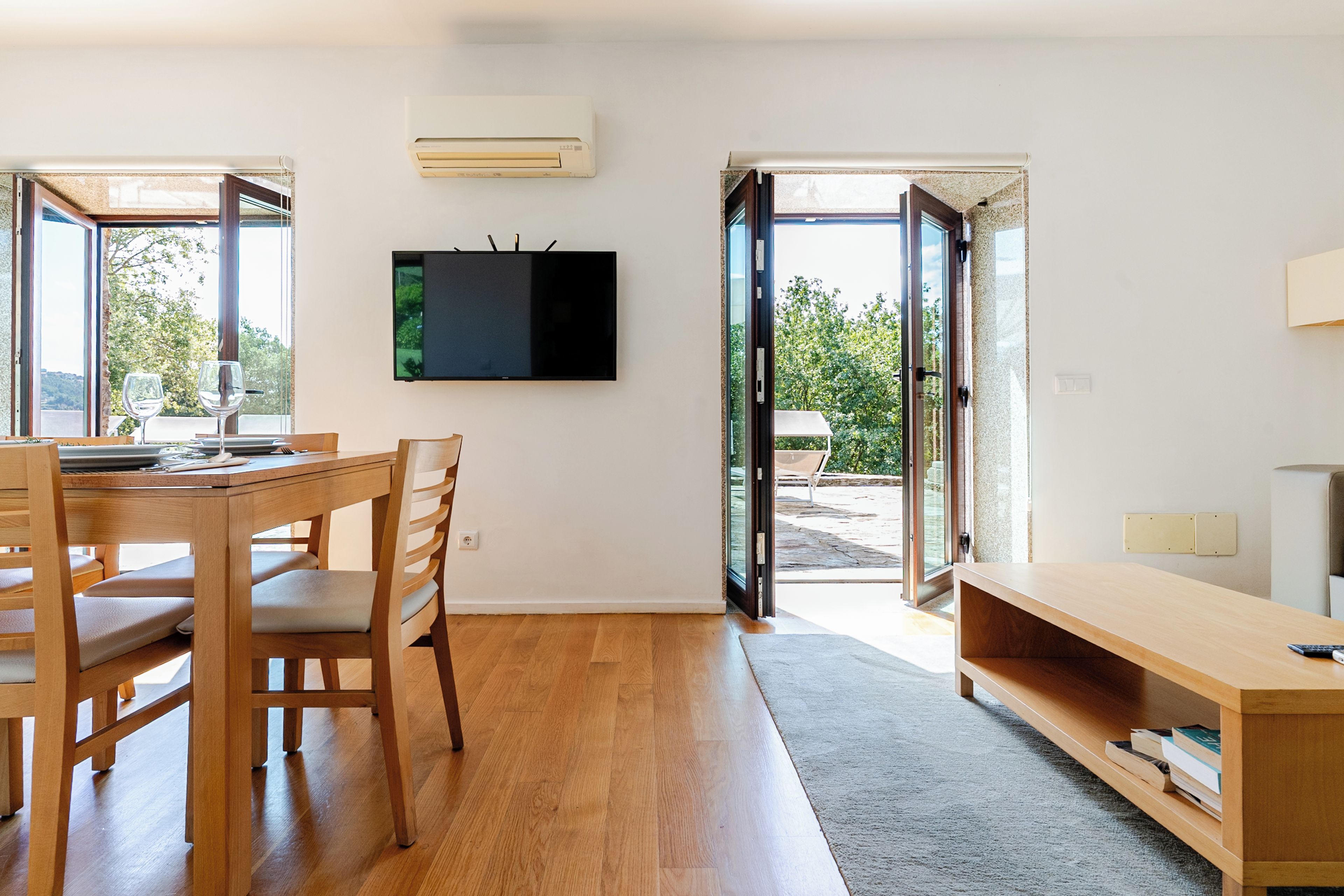 A modern interior with a dining area, a flat-screen TV mounted on the wall, and a sliding glass door leading to an outdoor patio.