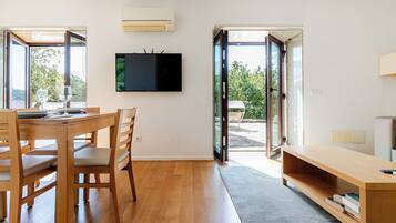 A modern interior with a dining area, a flat-screen TV mounted on the wall, and a sliding glass door leading to an outdoor patio.