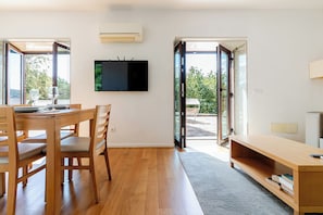 A modern interior with a dining area, a flat-screen TV mounted on the wall, and a sliding glass door leading to an outdoor patio.