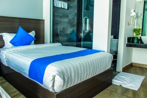 A neatly made bed with a blue accent, a glass shower door, a hairdryer on the wall, and a small plant on the bathroom counter. - Good Time Boutique Hotel (Sihanoukville)