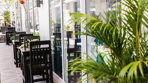 A restaurant with outdoor seating, glass walls, and potted plants. - Good Time Boutique Hotel (Sihanoukville)