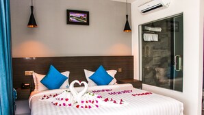 A hotel room with a large bed, two blue pillows, a heart-shaped decoration on the bed, and a shower area with a glass door. - Good Time Boutique Hotel (Sihanoukville)