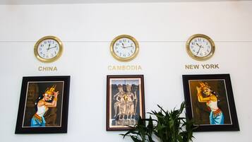 Three clocks labeled "CHINA," "CAMBODIA," and "NEW YORK" on a wall, each with a framed picture below.