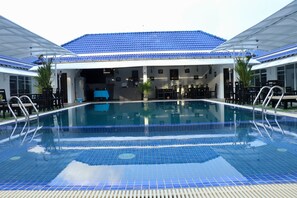 A swimming pool with a tiled deck, surrounded by outdoor seating and a covered area with a blue roof. - Good Time Boutique Hotel (Sihanoukville)