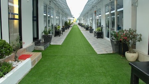 A corridor with artificial green carpet, potted plants, and outdoor seating areas. - Good Time Boutique Hotel (Sihanoukville)