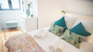 Una cama bien hecha con toallas enrolladas, una manta colorida y almohadas color turquesa.