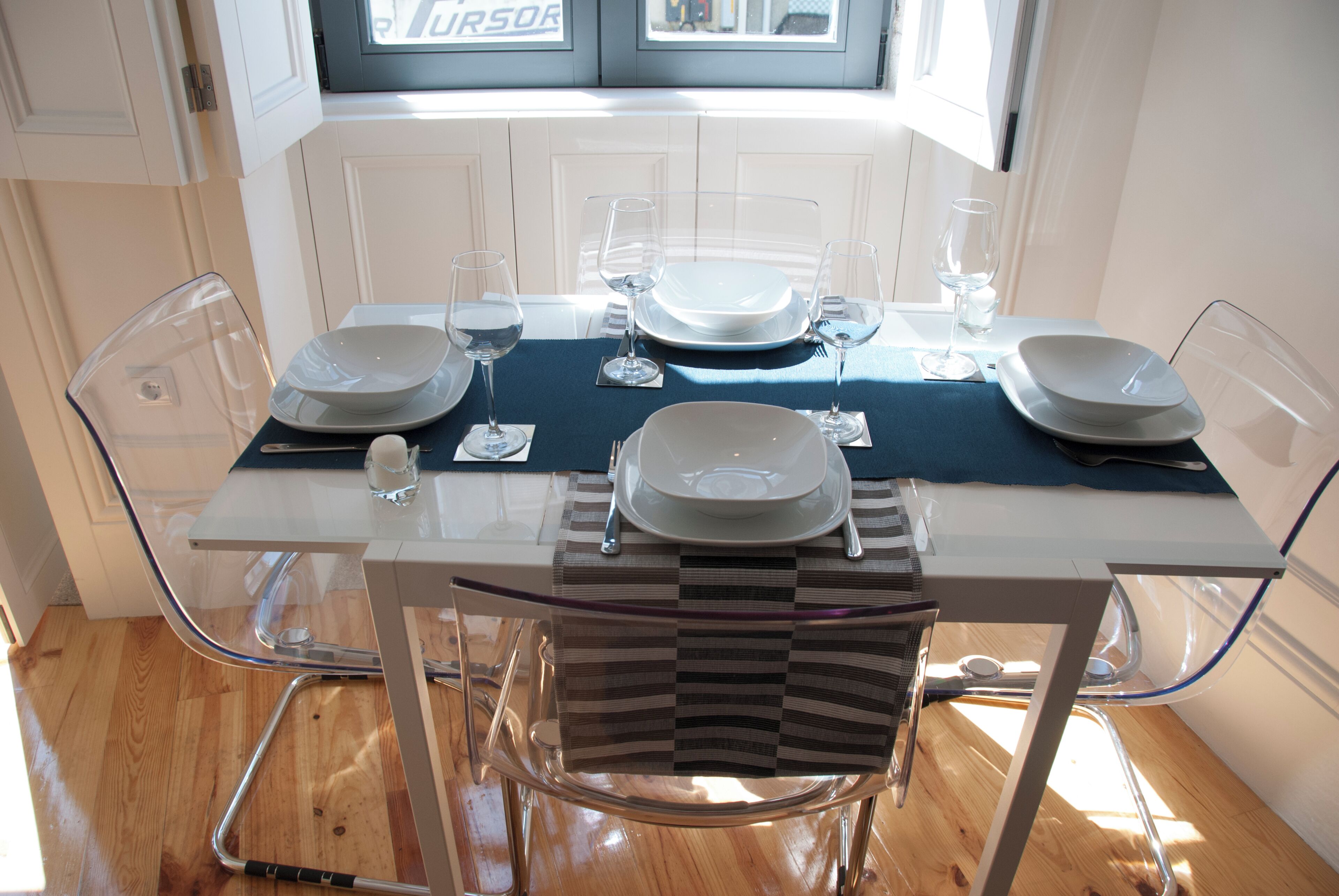 A dining table set with plates, glasses, and cutlery, surrounded by clear chairs.