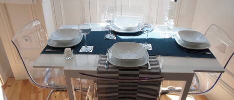 A dining table set with plates, glasses, and cutlery, surrounded by clear chairs.