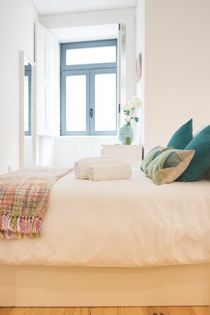 A bedroom with a bed, pillows, a vase with flowers, and a window.