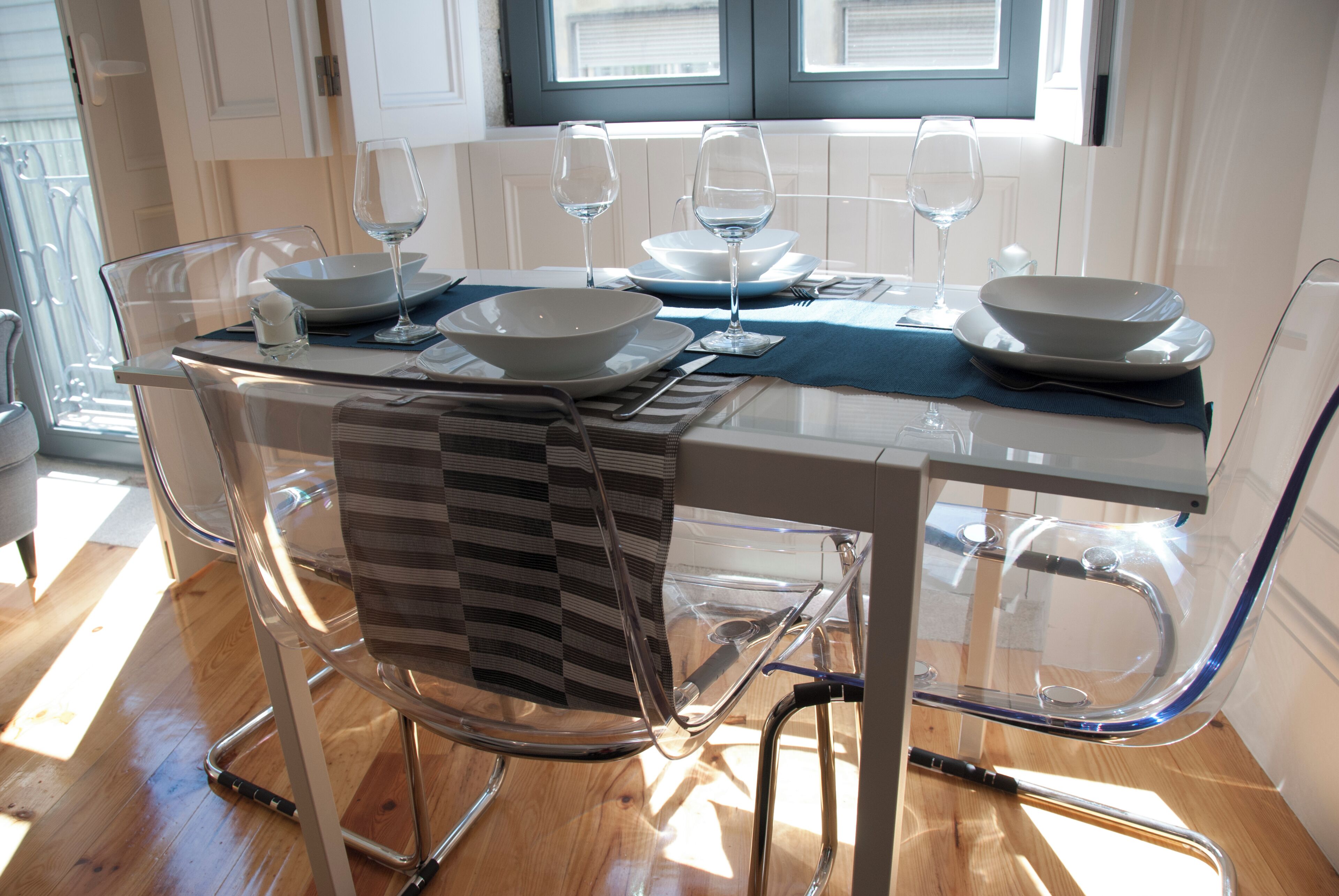A dining area with a glass table, chairs, and white plates with wine glasses.