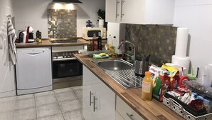 A modern kitchen with a dishwasher, oven, and microwave. There is a sink with a faucet and a dish rack. Various kitchen items and groceries are visible on the counter.