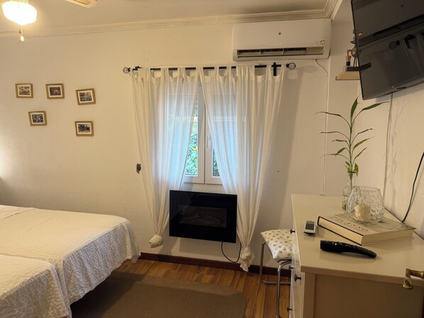 A room with a bed, a small table with a book and remote, a TV, and a window with curtains.