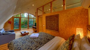 Quarto com cama grande, sofá e escrivaninha. Janelas amplas e vista para o exterior.