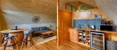 A compact living space with a wooden floor, a sofa, a dining table, and a kitchen area with a microwave and sink.