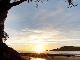 Escena de playa con atardecer, costa rocosa y una montaña a lo lejos.
