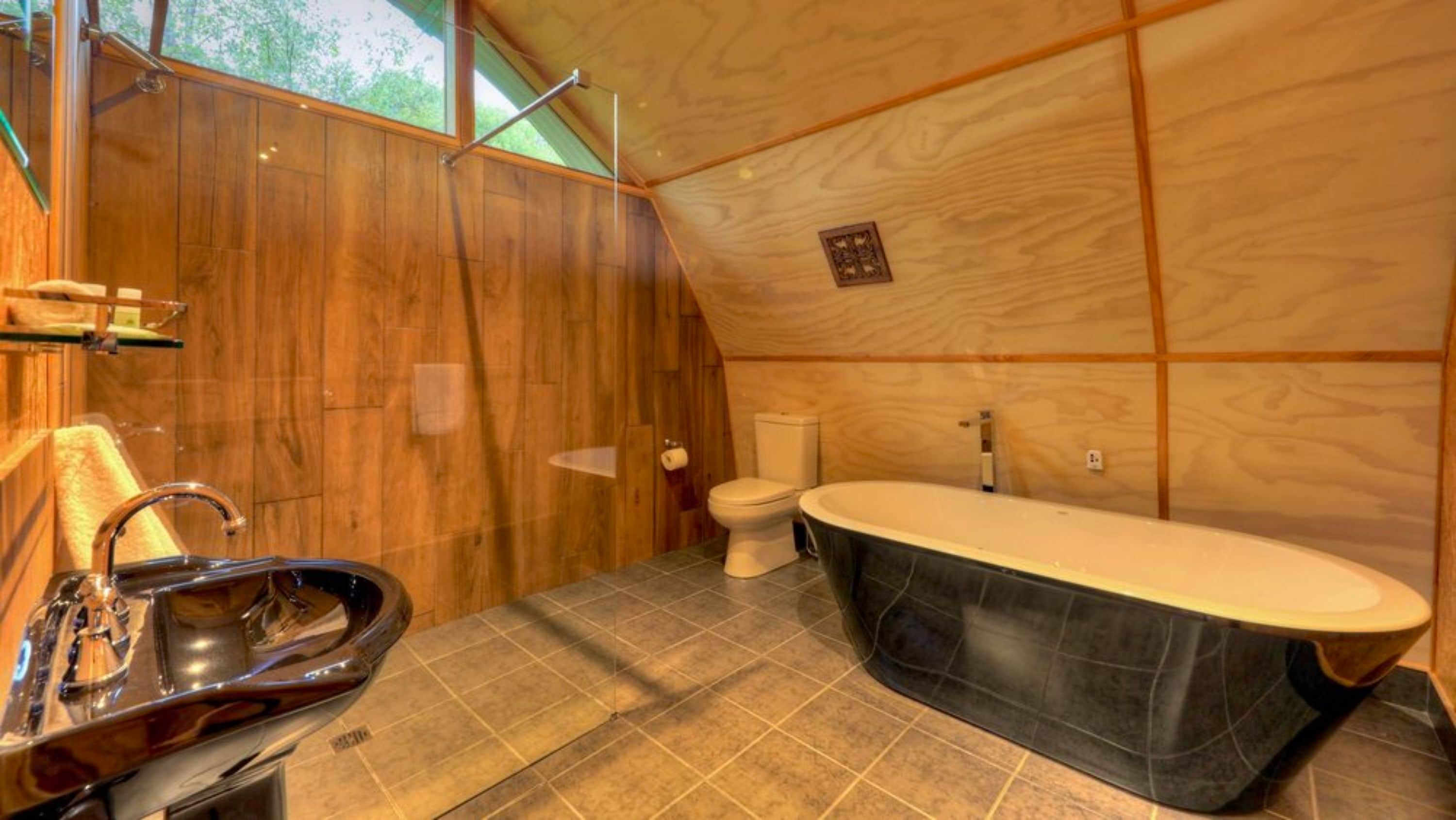 A compact bathroom with a wooden interior, a freestanding bathtub, a sink, and a toilet.