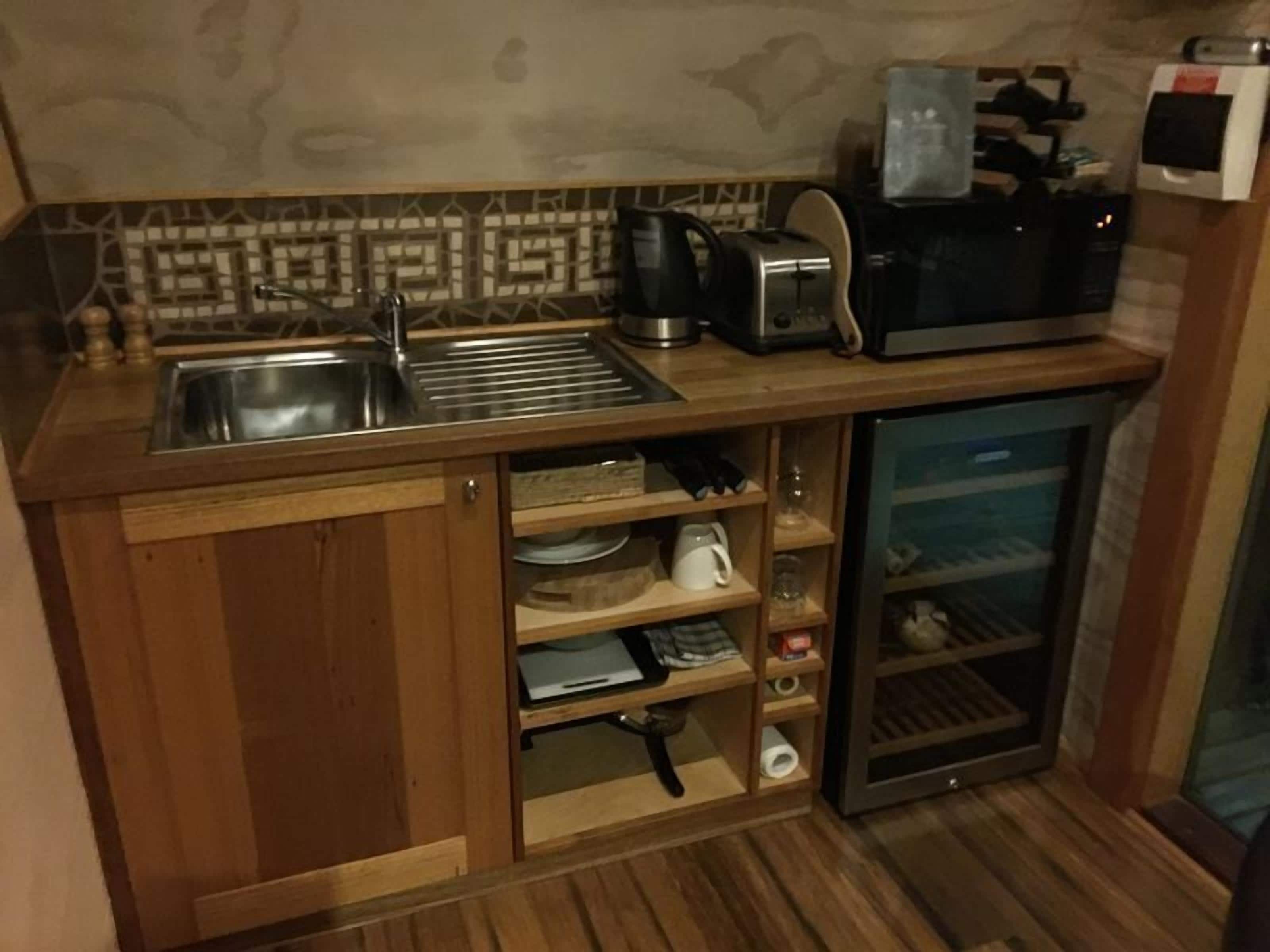 A compact kitchen with a sink, toaster, kettle, and a small refrigerator.