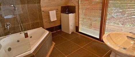 Un baño con bañera, lavamanos y ventana con persianas.