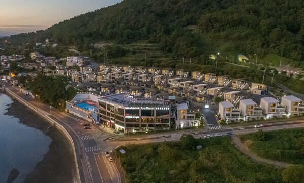 Vista aérea de un complejo turístico con varias edificaciones, una piscina y una carretera con vehículos.