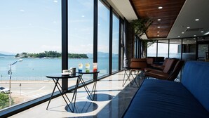 Quarto moderno com uma grande janela com vista para um corpo d'água, um sofá azul e uma pequena mesa com bebidas.